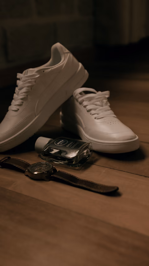 Sneakers, a watch and cologne arranged on a wooden floor